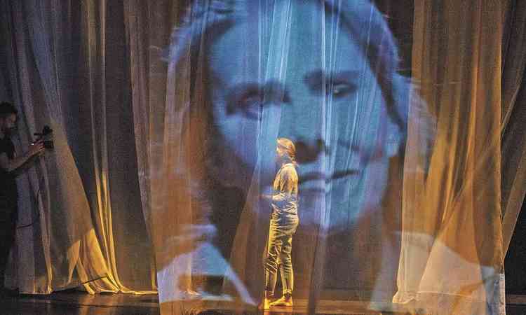 Mait Proena est no palco, descala e de cala comprida, atrs de cortina de voal
