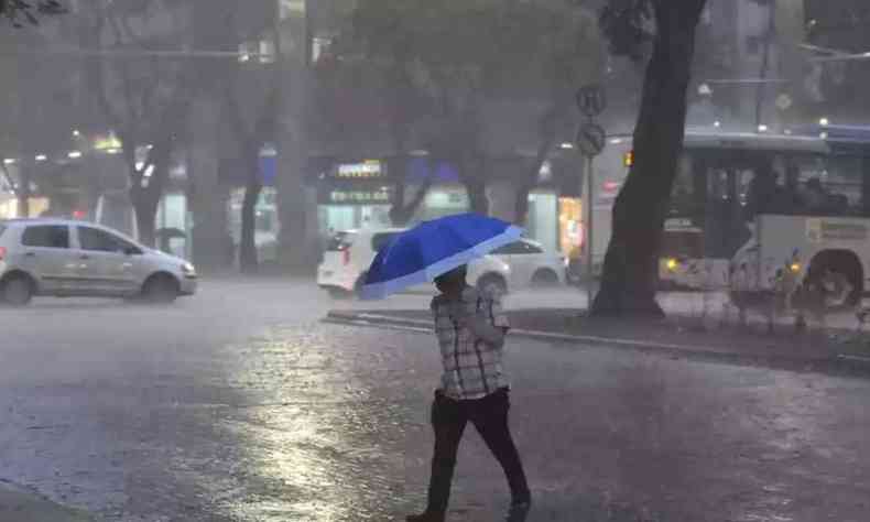 Homem atravessa rua durante chuva com sombrinha. 