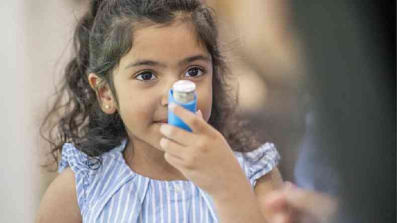 Menina criana segurando bombinha de asma em frente ao rosto
