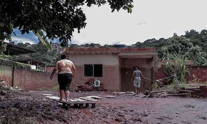 foto mostra barracão tomado por lama e moradores andando perto dele em Sabará