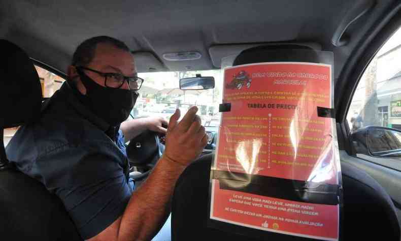 Marcelo, motorista de Uber, sentado ao volante, mostra o cartaz colado atrs do banco do passageiro 