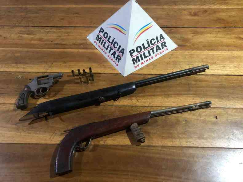 Armas de fogo em cima de uma mesa, ao lado do smbolo da Polcia Militar