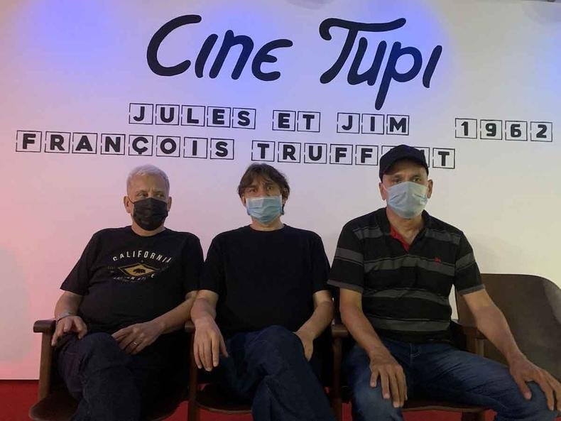 Os irmãos Borges, Márcio, Lô e Telo, na exposição 'Viagem de ventania - Trilha sonora do tempo', na Galeria de Arte do Centro Cultural Unimed-BH Minas(foto: Camila de Avila Alves/Divulgação) Os irmãos Márcio, Lô e Telo Borges sentados no sofá e usando máscaras, tendo ao fundo projeção onde se lê Cine Tupi, Jules et Jim, 1962, François Truffaut