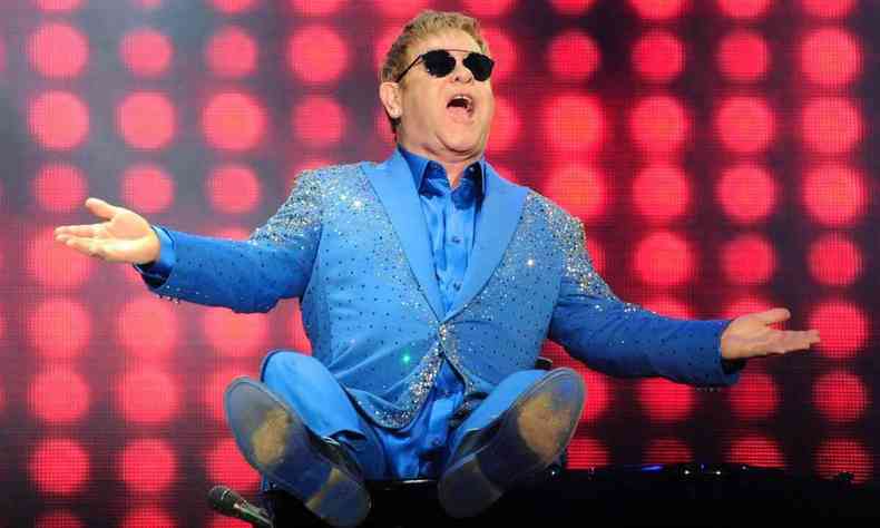 Elton John em cima do piano durante o Rock in Rio, com os braos abertos