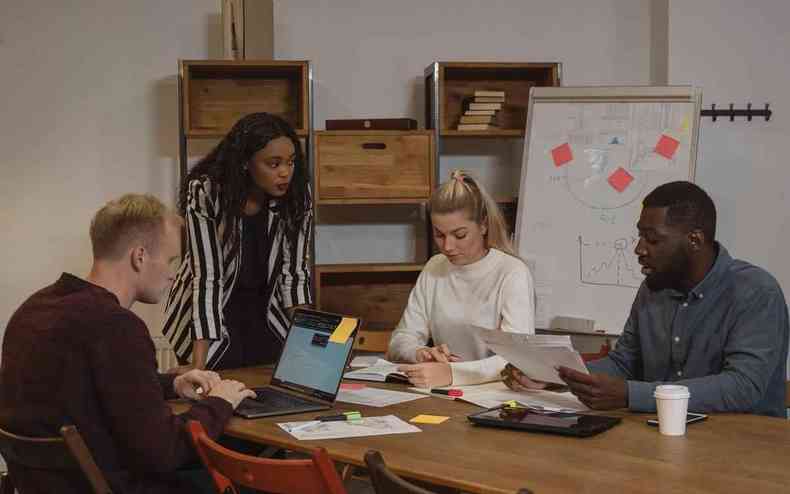 Foto de pessoas sentadas em uma mesa de reunio, um homem branco, uma mulher negra, uma mulher branca e um homem negro