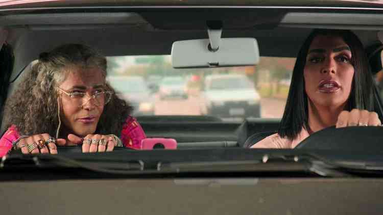 Caracterizado como Dona Isadir, Rodrigo Sant'anna anda no banco do passageiro de um carro dirigido por  Pepita, em cena 'A sogra que te pariu' (Netflix), 

