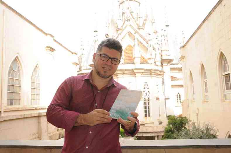 O padre Marcelo Souza segura um exemplar de seu livro de poemas em frente  Igreja Boa Viagem