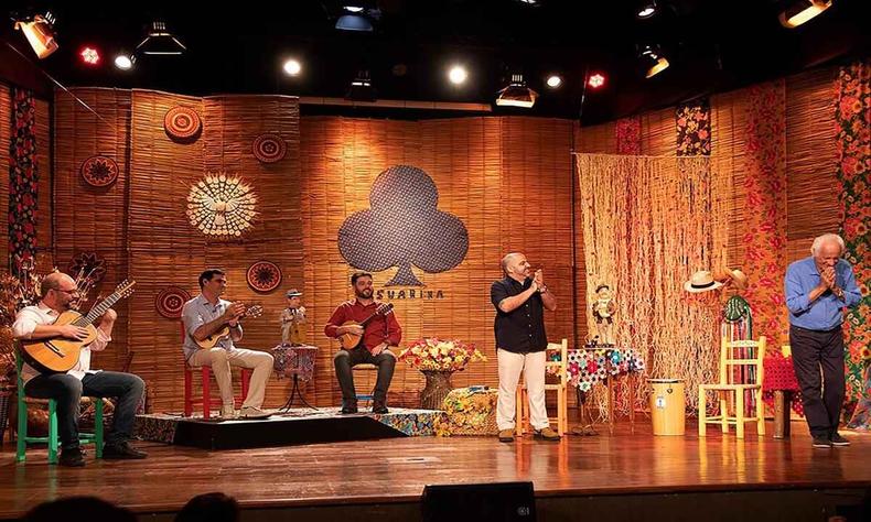 em palco decorado com objetos de palha, os integrantes do Casuarina, sentados, aplaudem Rolando Boldrin, que agradece curvando a cabea, de p