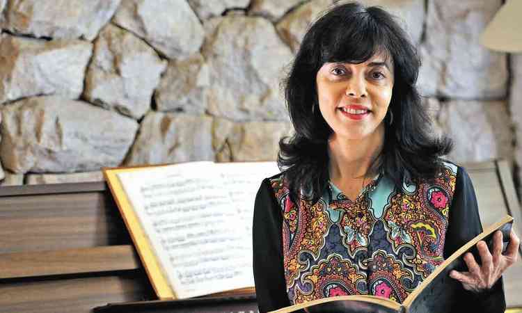 Professora de msica da UFMG Betnia Parizzi, sentada ao piano, sorri e tem livro nas mos