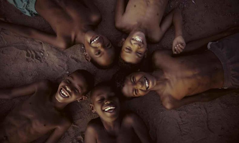Deitadas formando um crculo, crianas sorriem para a cmera