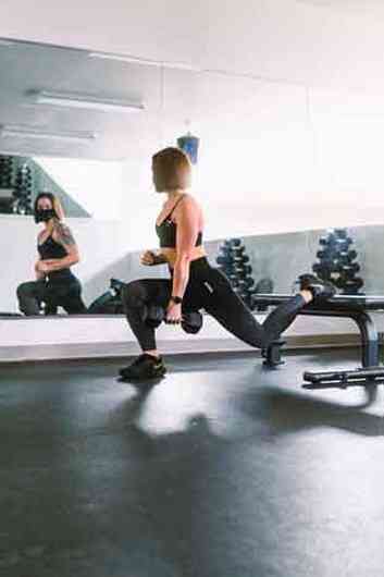 Mulher faz exerccio com um peso na academia, em frente ao espelho