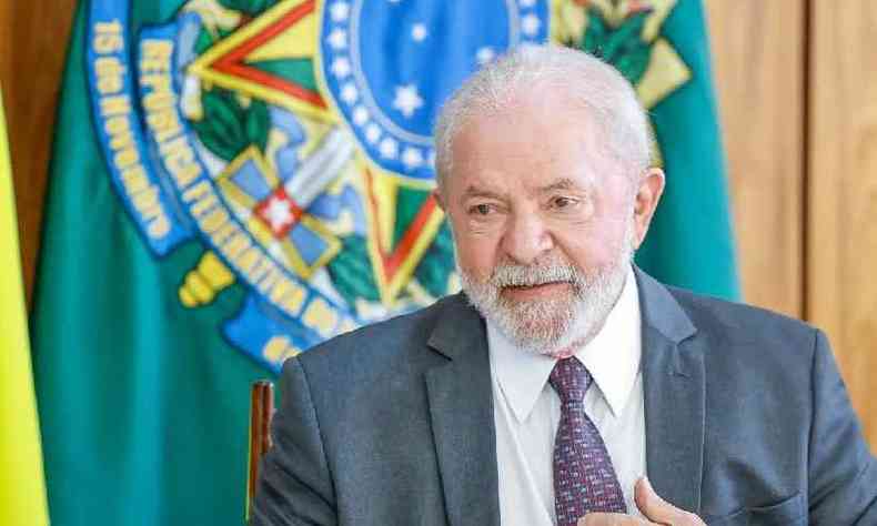 Presidente Lula em frente a uma bandeira-insgnia da Presidncia. Ele usa um terno cinza, uma camisa branca e uma gravata cinza, azul marinho e vermelha