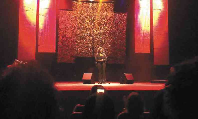 Cantora Margareth Menezes, vestindo cala e blusa pretas, est em p sob a luz vermelha, no palco do Sesc Palladium