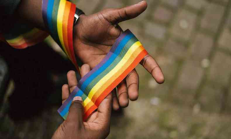 Mãos de uma pessoa negra segurando uma fita com as cores do arco-íris