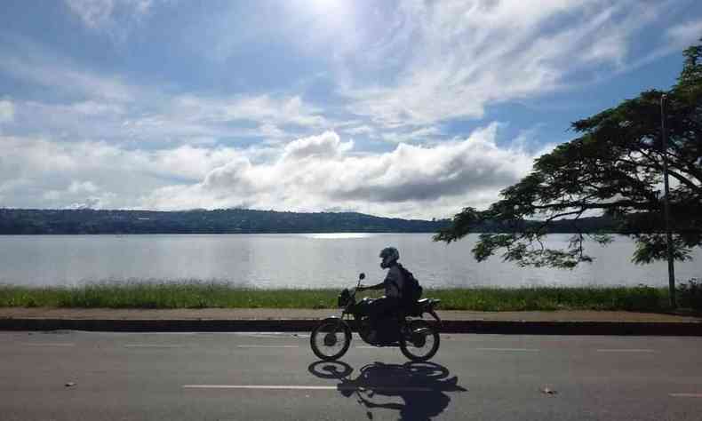 Moto andando na orla da Lagoa Central, em Lagoa Santa, com sol forte e poucas nuvens.