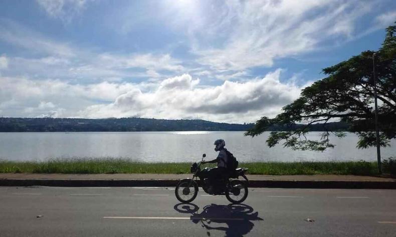 Moto andando na orla da Lagoa Central, em Lagoa Santa, com sol forte e poucas nuvens.