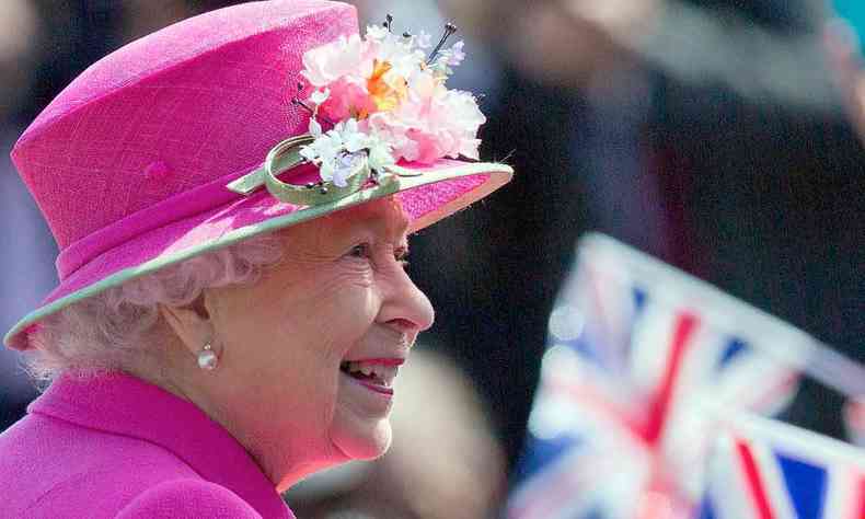 Rainha Elizabeth, usando chapu rosa, sorri 