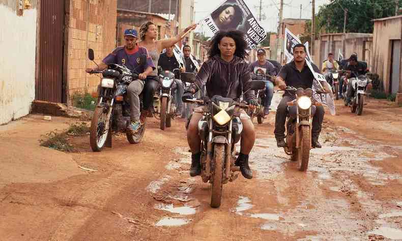 Grupo de mulheres de moto carrega faixa e trafega em rua de periferia no filme Mato seco em chamas