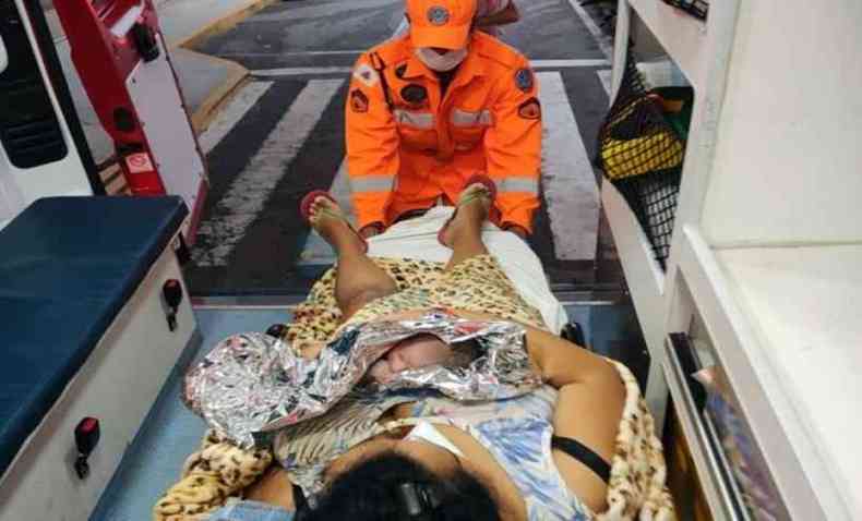 Mulher sendo atendida por um agente do corpo de bombeiros dentro da ambulncia; ela segura o beb no colo 