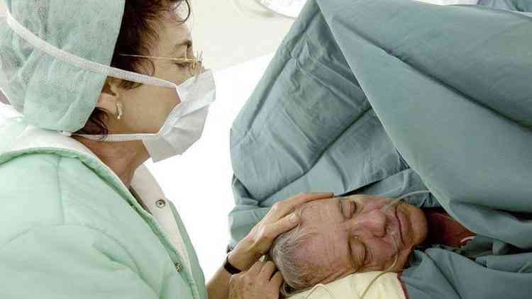 Mulher de mscara colocando a mo sobre a cabea de paciente sedado - cirurgia sob hipnose na Blgica