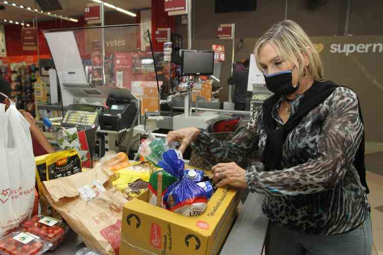 Mulher de roupa preta na fila do caixa de supermercado, fazendo compras de diversos alimentos que esto juntos em uma caixa de papelo