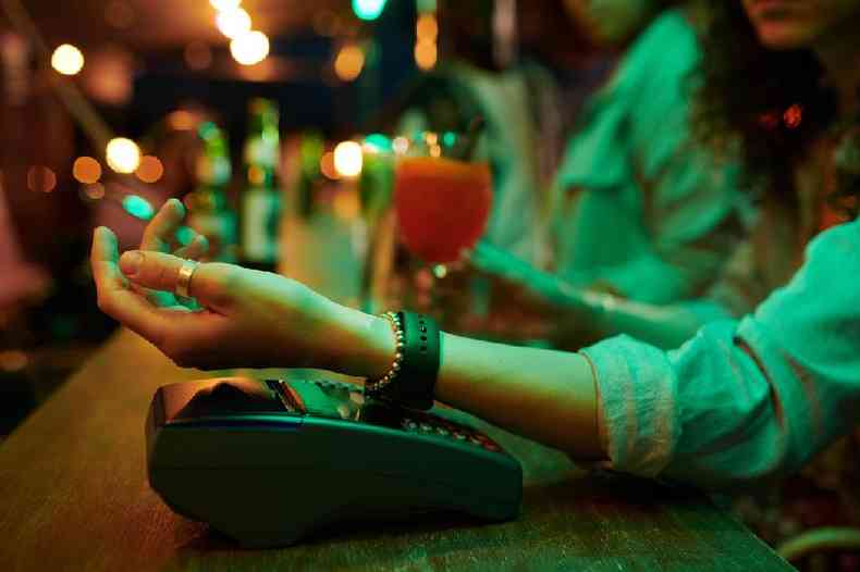 Mulher fazendo pagamento com smartwatch em balco de bar