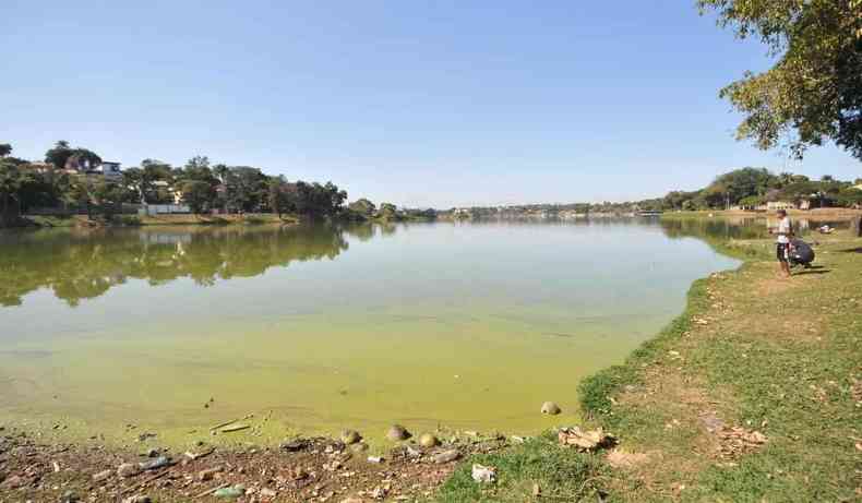 Lagoa poluida, com superfcie verde. Homem pescando ao lado.