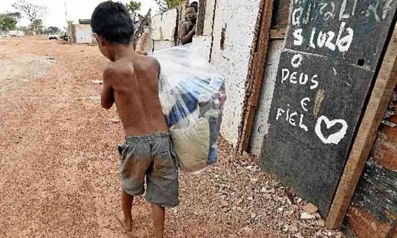Na foto, menino carrega sacola em área de pobreza