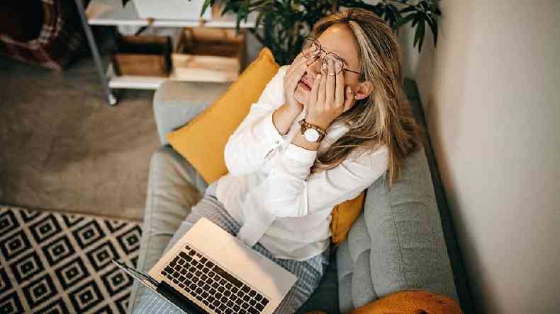 Mulher cansada trabalhando com laptop no colo no sof de casa