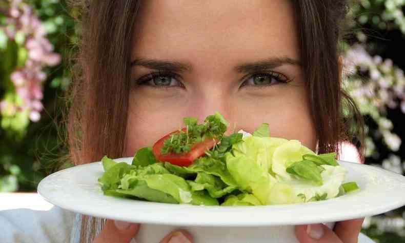 mulher com prato de salada , segurando no alto, em frente aos nariz