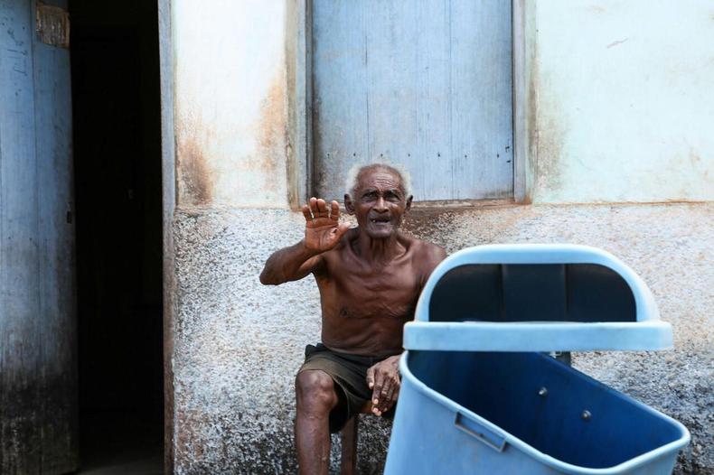 Idoso acena, sentado na porta de casa