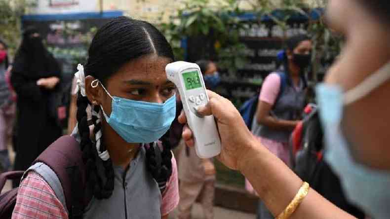 Uma professora verifica a temperatura de uma menina quando ela chega para assistir s aulas aps a reabertura das escolas fechadas como medida preventiva para conter a propagao da covid-19, em uma escola em Madurai em 01 de fevereiro de 2022