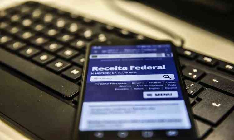 Imagem de um celular em cima de um teclado de computador na tela do site da Receita Federal
