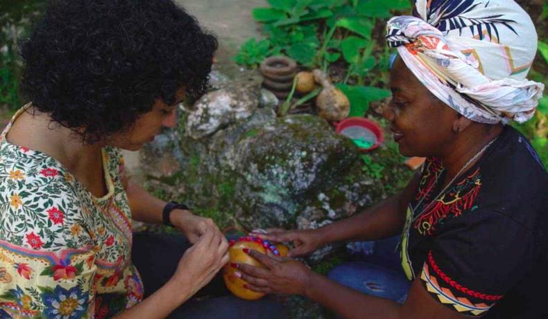 No quilombo de Rodrigues, o visitante é convidado a confeccionar seu próprio xequerê.(foto: Instituto Rede Terra/Divulgação) Duas mulheres fazendo o instrumento.