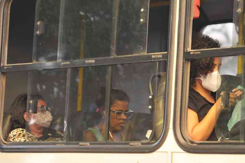 Pessoas na janela do ônibus, algumas com máscara, outra sem