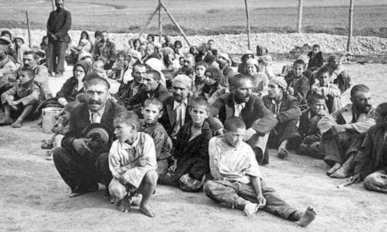 Fotografia em preto e branco de um grupo de ciganos sentados no cho, presos em um campo de concentrao nazista