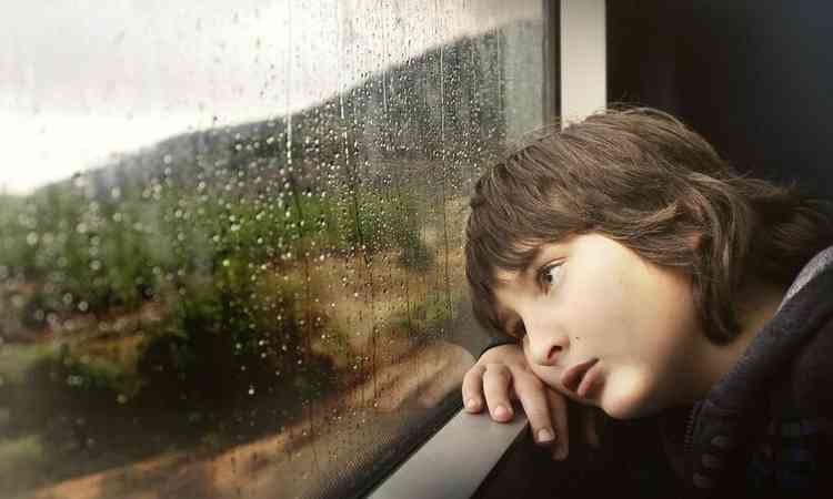 um menino triste com a cabea apoiada na janela