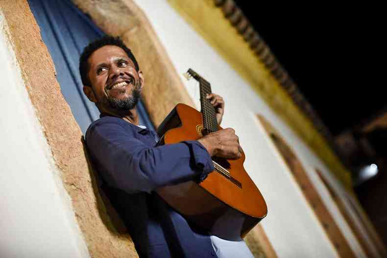 Segurando o violo, Miguel dos Anjos sorri, em frente a uma casa colonial tpica de Minas Gerais