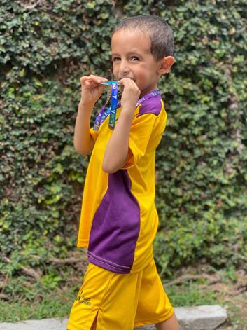 Menino pardo com medalha no pescoo uniforme amarelo e roxo