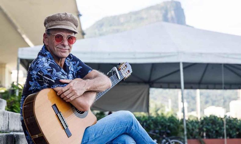 Cantor, compositor, baixista e produtor Rodrigo Santos est sentado, abraado ao violo, ao fundo v-se o perfil do Corcovado, no Rio de Janeiro