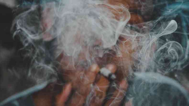 Homem fumando com fumaa em frente ao seu rosto