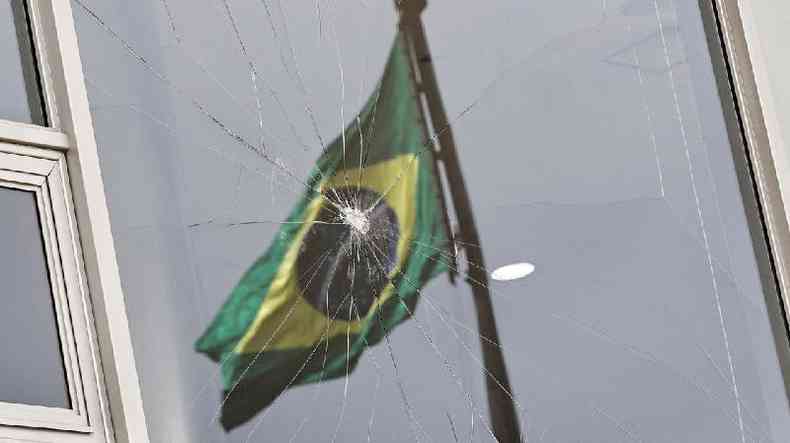 Imagem mostra bandeira do Brasil refletida com janela quebrada