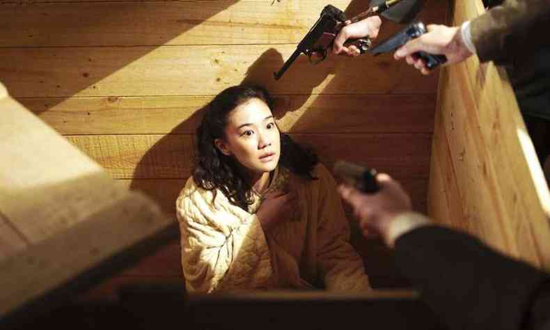 Mulher japonesa encolhida e apavorada est sentada e olha para armas apontadas para ela