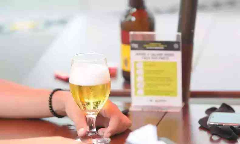 Na foto, pessoa em um bar segurando uma taa de cerveja
