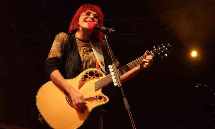 Rita Lee em apresentao. Ela tem os cabelos vermelhos com uma franja e segura uma guitarra.