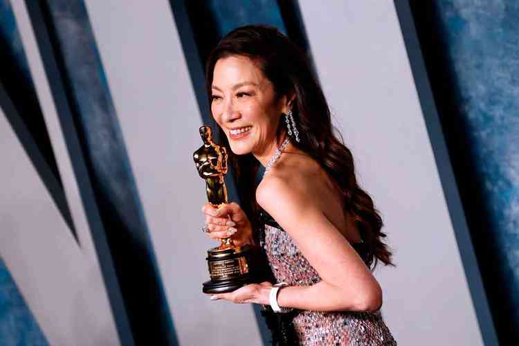A atriz Michelle Yeoh segura sua estatueta e sorri, enquanto posa para fotos
