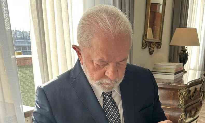 O presidente Lula olha concentrado para baixo. Ele veste um terno azul e uma gravata azul-marinho com listras cinza, preto e branco