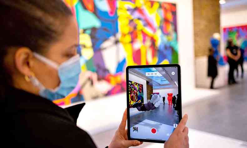Mulher acessa aplicativo do celular que lhe permite ver obra do artista Kaws que está invisível a olho nu na galeria Serpentine