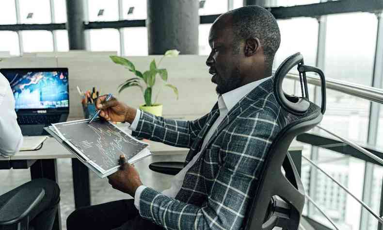 Homem negro usando um terno escuro xadrez analisa uma planilha com um grfico em um escritrio