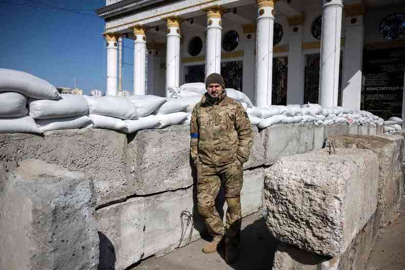 De uniforme militar, de pé, em frente a construção com colunas brancas, o cineasta Oleg Sentsov olha para a câmera
